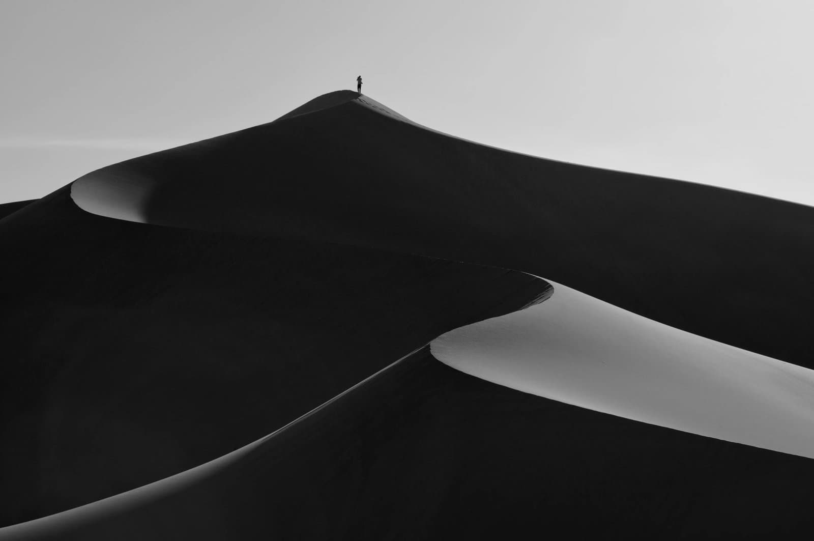 A person standing on top of a stand dune in the desert