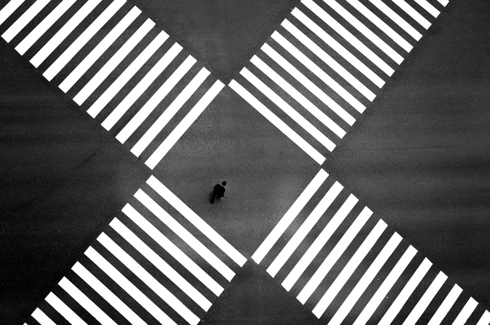 Aerial view of a single person standing at the centre of intersecting pedestrian crossings