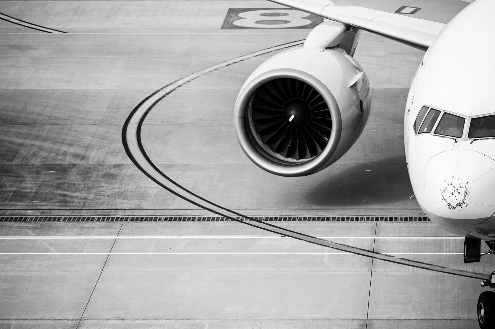 Close-up of a commercial aircraft parked on an airport apron, showing the engine, wing and nose section.