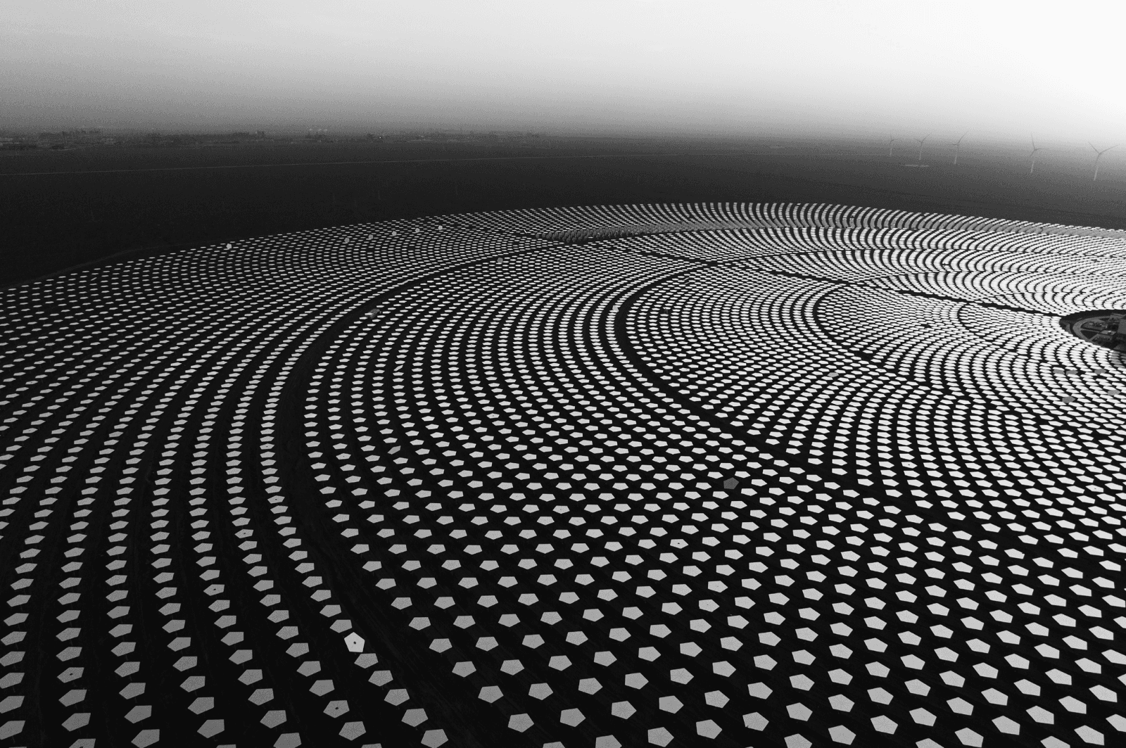 Hexagonal solar panels with wind turbines in the distance