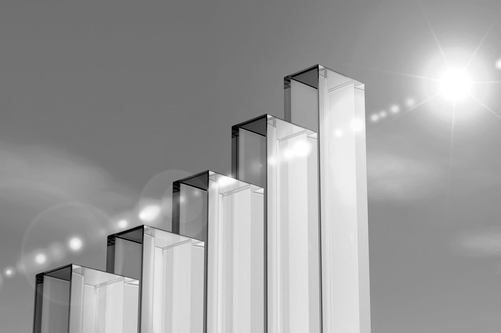 Glass bars arranged in ascending height like a chart, illuminated by sunlight against a clear sky.