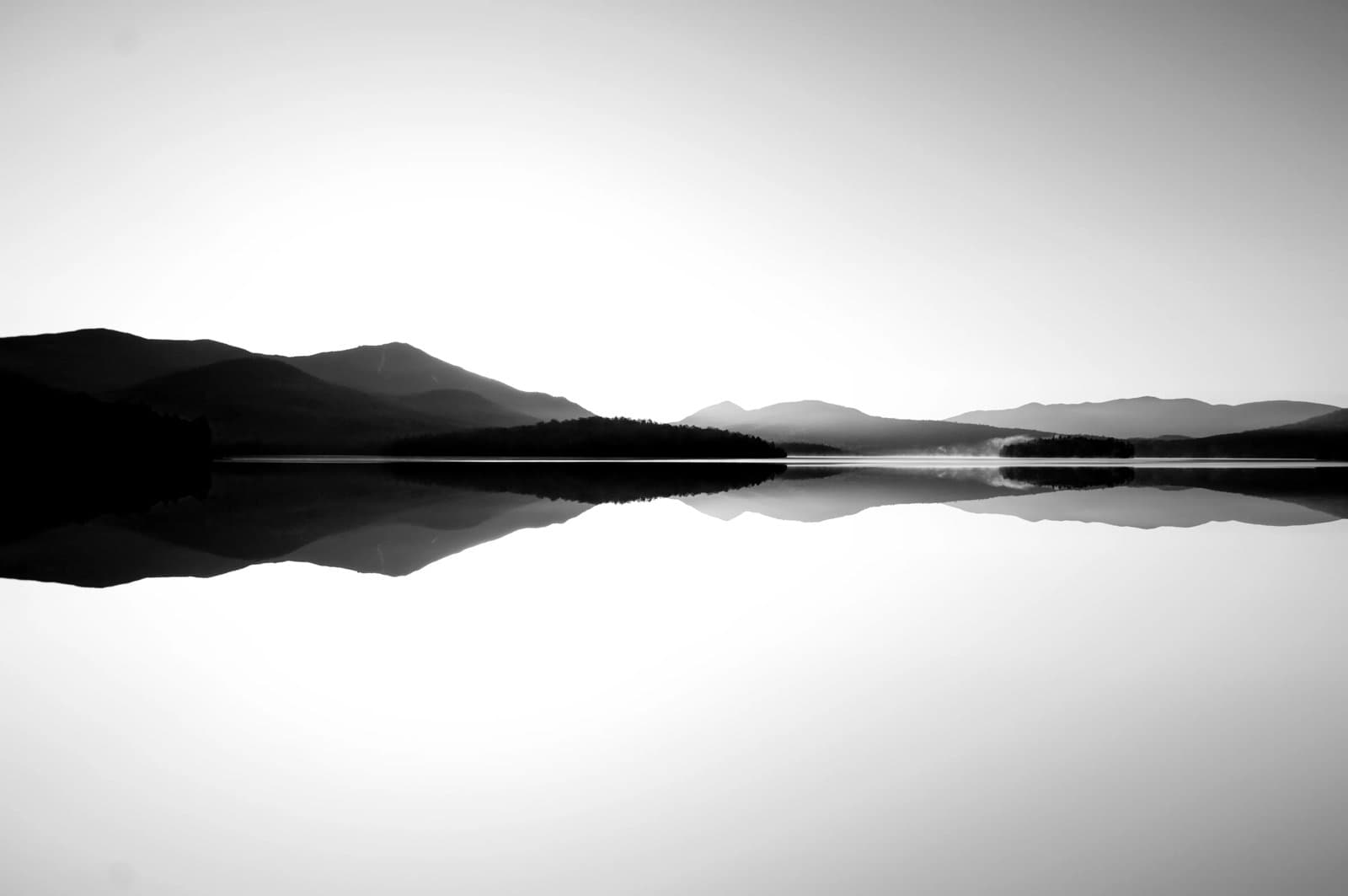 Calm lake reflecting distant mountains at sunrise or sunset.