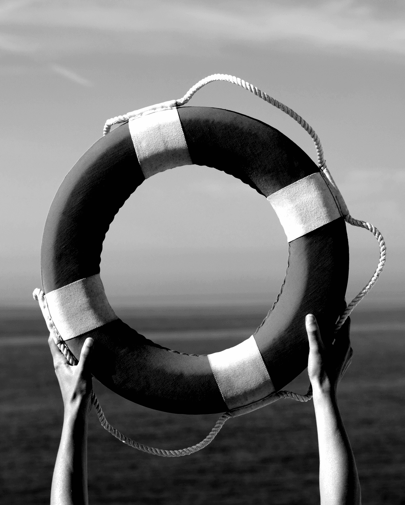 Hands holding a life preserver ring with rope against ocean and sky in black and white.