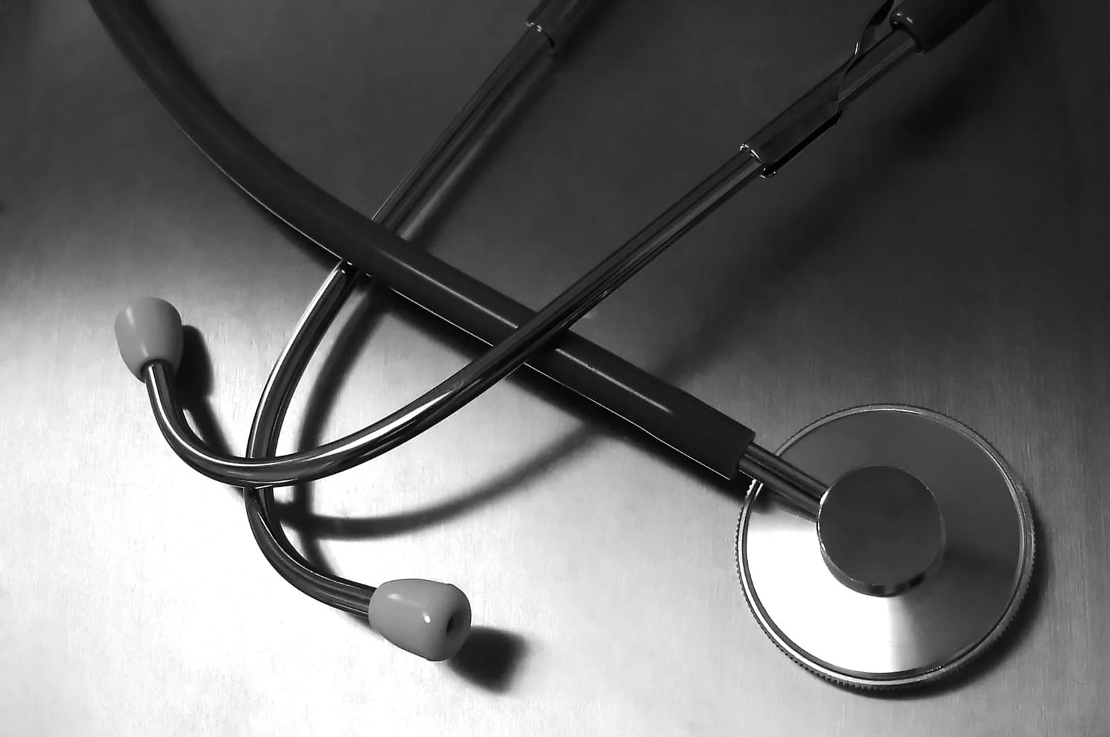 Close-up of a black stethoscope resting diagonally on a brushed metal surface.